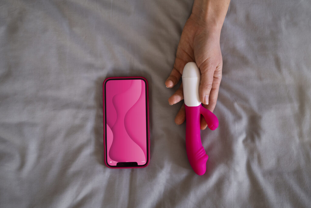 Appstyrt vibrator og mobiltelefon på seng – moderne sexleketøy for par og solo-lek med kontroll via app.